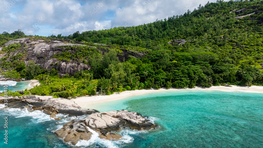 Granite rocks jut out from a pristine white beach, with dense green foliage. Therese. Seychelles, Mahe. Granite rocks jut out from a pristine white beach, with dense green foliage. Therese. Seychelles, Mahe.