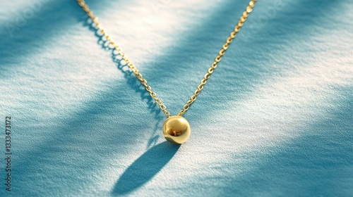 A minimalist gold necklace with a subtle shine on a soft pastel blue background.