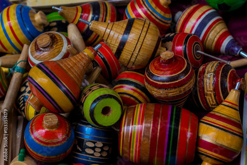 Close up of collection of colorful traditional wooden spinning tops with vibrant striped patterns in a market stall, selective focus, trompos