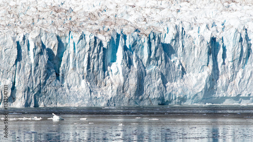 The image captures the stunning majesty of a towering glacier, with its blue and white hues reflecting in the calm waters below, illustrating the beauty of nature’s frozen wonders.