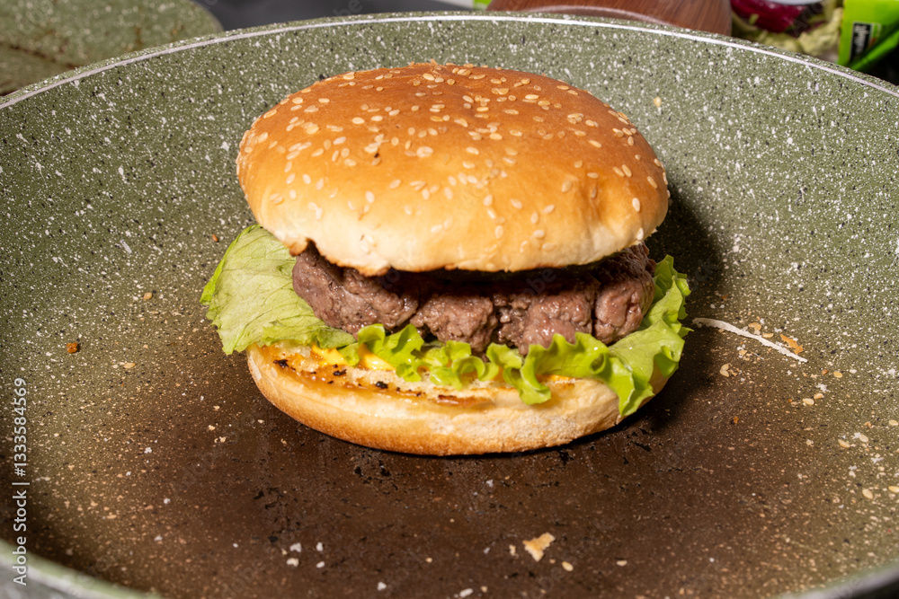 A fresh sesame seed hamburger bun with beef patty, lettuce, and sauce rests on a griddle, showcasing a classic burger ready to enjoy.