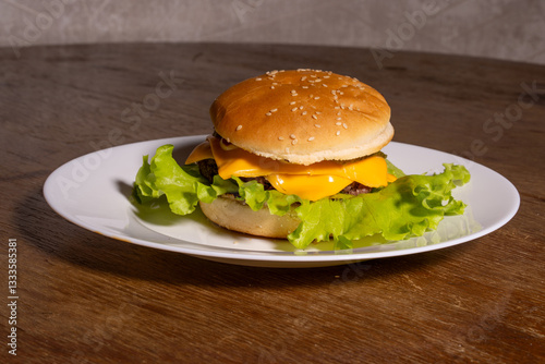 Obraz na płótnie A juicy cheeseburger with a sesame seed bun, melted cheese, beef patty, and lettuce on a white plate, styled atop a rustic wooden background. w salonie