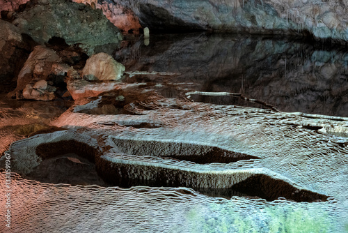 Tableau sur toile The image captures an intriguing underground cave with stunning stalactite formations reflected in still water, showcasing nature's artistry in a serene environment