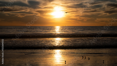 The peaceful image of a sunset cast over calm waters, showcasing soft golden hues contrasted against the light clouds, represents serenity and the beauty of nature.