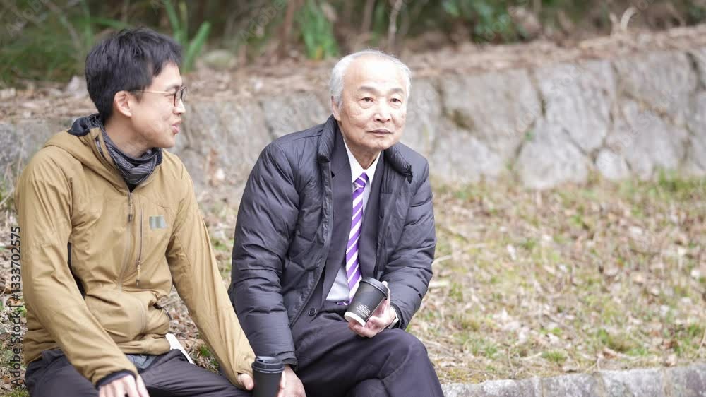 A Japanese winter daytime park. A 78-year-old Japanese man in a suit and a down jacket is sitting on concrete. My son, in his 30s, brings me a paper cup of coffee and drinks it together.