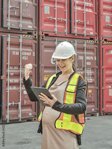 Healthy pregnant woman working under safety supervision and health insurance in industrial plant doing field work in storage yard and packing empty containers for shipping. Working safely in outdoor 