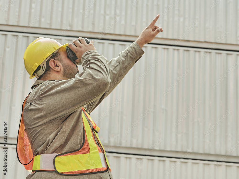 Construction worker in safety gear wearing a virtual reality headset and pointing, standing in front of an industrial building or warehouse structure