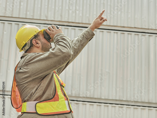 Obraz na płótnie Construction worker in safety gear wearing a virtual reality headset and pointing, standing in front of an industrial building or warehouse structure w salonie