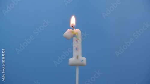Burning white birthday candle on blue background, number 1.	