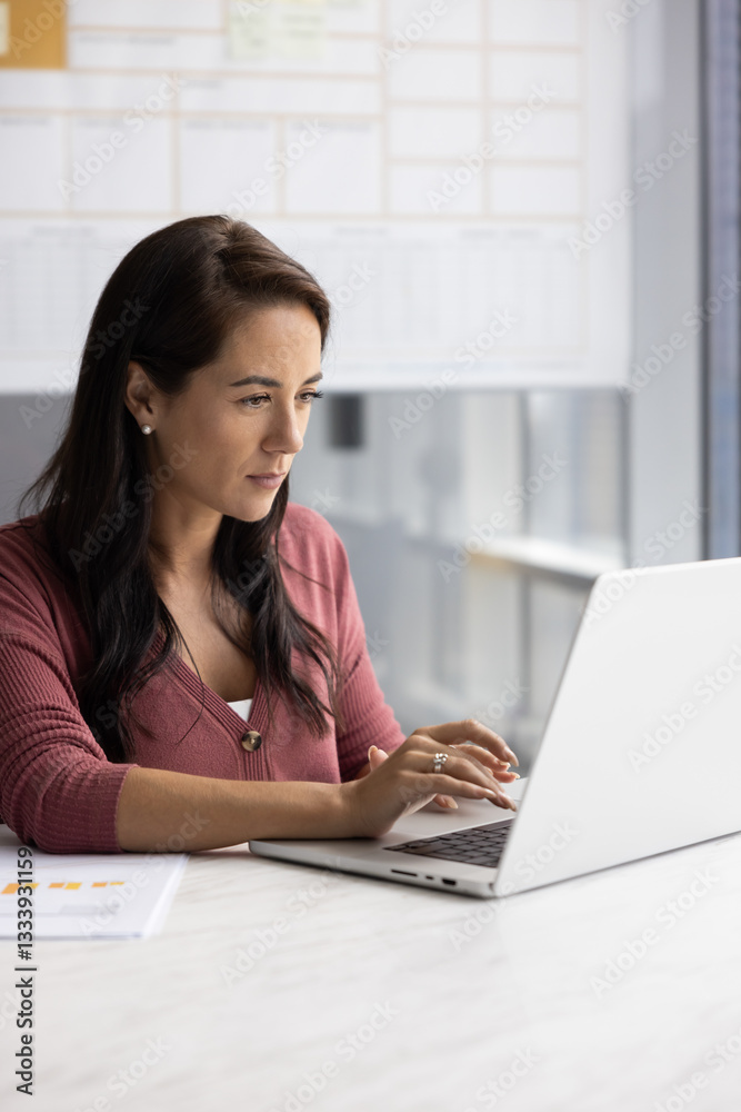 Focused Hispanic businesswoman typing on laptop in office, working on online marketing strategy, product promotion on social media. Project manager using computer. Vertical shot Focused Hispanic businesswoman typing on laptop in office, working on online marketing strategy, product promotion on social media. Project manager using computer. Vertical shot