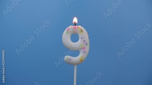 Burning white birthday candle on blue background, number 9.	