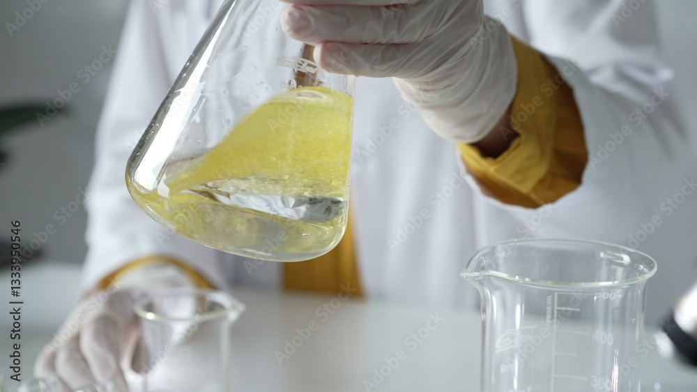Unknown scientist wearing white protective gloves is carefully shaking up a yellow chemical solution inside an Erlenmeyer flask in a laboratory, close up. Science and medicine