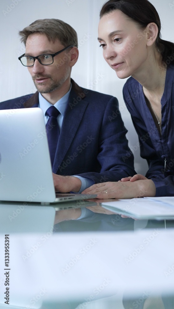Two professionals collaborating in a modern office setting, using a laptop and discussing a project, vertical portrait. Business people concept