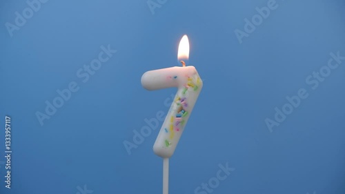 Burning white birthday candle on blue background, number 7.	