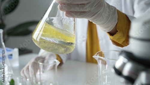 Obraz na płótnie Unknown scientist wearing white protective gloves is carefully shaking up a yellow chemical solution inside an Erlenmeyer flask in a laboratory, close up. Science and medicine w salonie