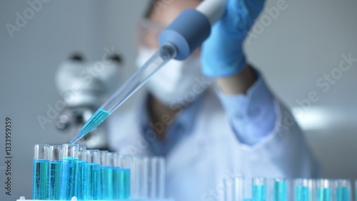 Close up of a female scientist researcher hand using a micropipette to fill up test tubes with a blue liquid in laboratory. Medicine and science