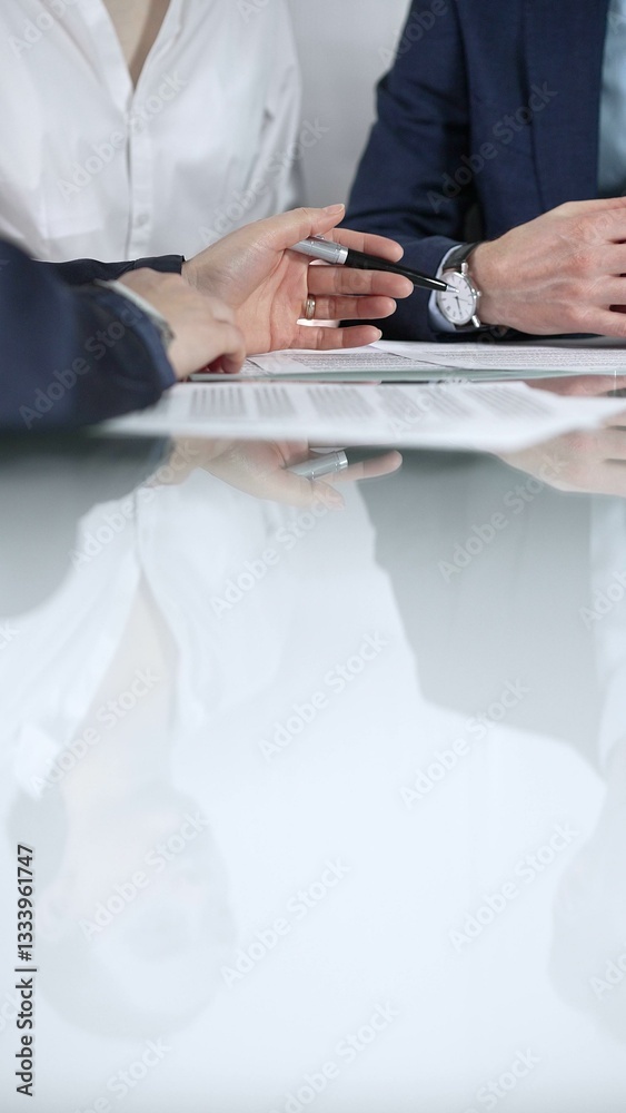 Unrecognizable business people are reviewing contract terms during a meeting while sitting at the glass table in office, vertical close up view. Copy space area