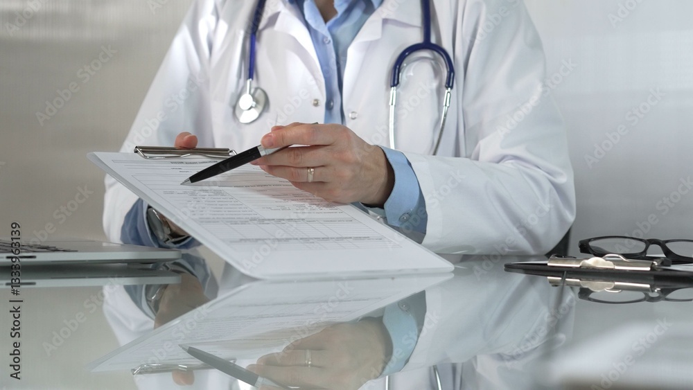 Female doctor, wearing a blue blouse under a medical coat, is pointing at medical chart, showcasing expertise in a close up shot. Medicine concept