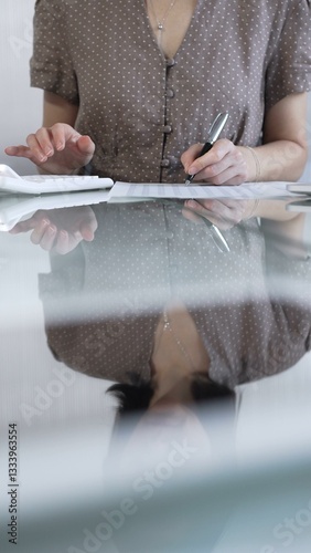 Obraz na płótnie Businesswoman accountant, wearing brawn dotted blouse, is using a calculator at sleek glass desk in a contemporary office, vertical view. Taxes, audit in business w salonie