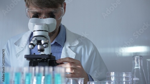Obraz na płótnie A man scientist, wearing a lab coat, mask, and safety glasses, is using a microscope surrounded by test tubes in laboratory setting. Medicine and science concept w salonie