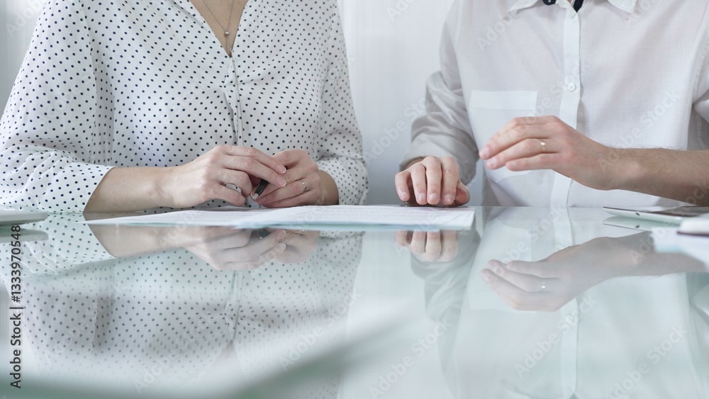 Business colleagues reviewing a contract, engaging in negotiations and strategic decision making in modern glass office, white casual dress style. Businesspeople concept