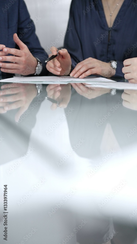 Unrecognizable business people are discussing a contract during meeting while sitting at the glass table in office, vertical close up view. Copy space area