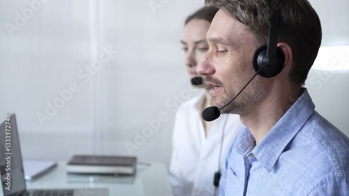 Happy smiling male call center operator in blue casual shirt is assisting clients online, providing customer support and answering inquiries. Business call center