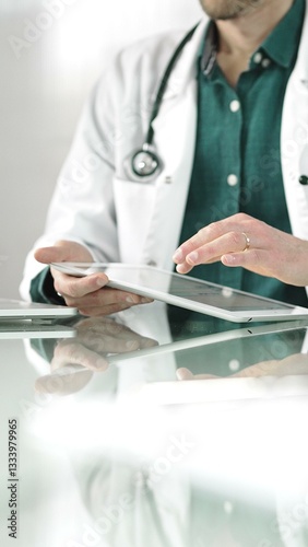 Obraz na płótnie Doctor man in green shirt under a white coat using digital tablet in modern healthcare setting, interacting with patient data. Medicine concept w salonie