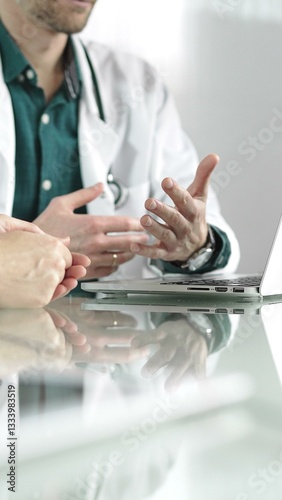 Obraz na płótnie Doctor man wearing a stethoscope and lab coat is gesturing with hands while explaining a diagnosis to a patient across a desk with a laptop. Medicine concept w salonie