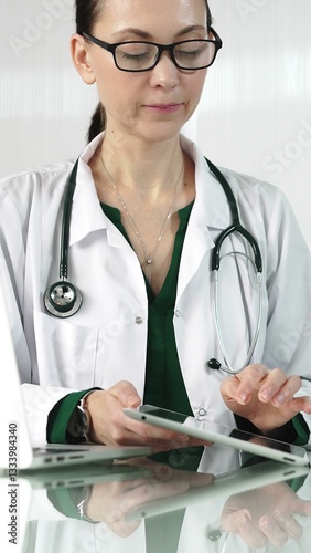 Obraz na płótnie Female doctor in white coat using digital tablet in modern healthcare setting, interacting with patient data, vertical portrait. Medicine concept w salonie