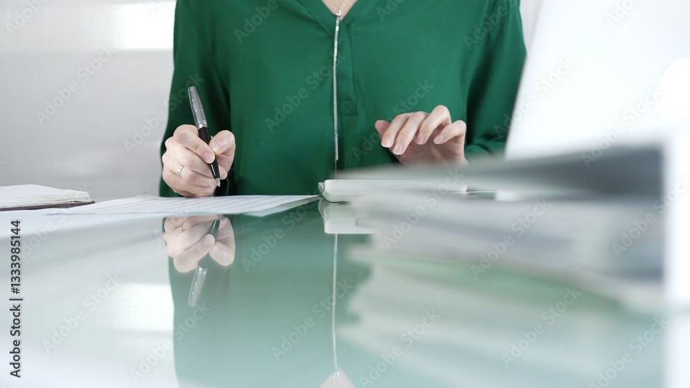 Businesswoman accountant at a sleek glass desk in a contemporary office, using a calculator to crunch numbers and jotting down meticulous notes, green color style. Taxes, audit in business