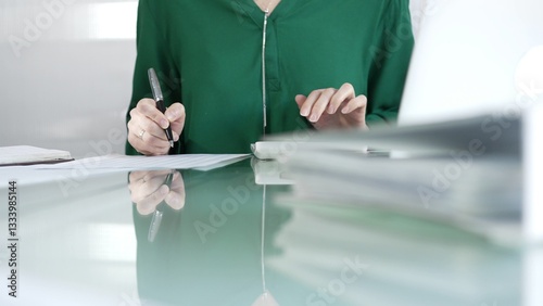 Obraz na płótnie Businesswoman accountant at a sleek glass desk in a contemporary office, using a calculator to crunch numbers and jotting down meticulous notes, green color style. Taxes, audit in business w salonie