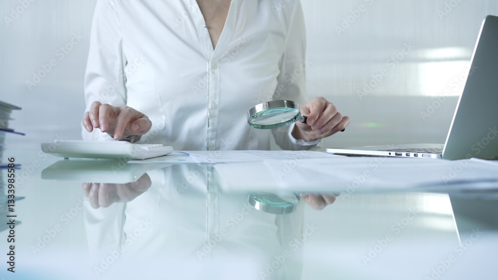 Businesswoman analyzing financial data with magnifying glass and calculator, performing accounting and auditing tasks in office. Audit and taxes theme in business