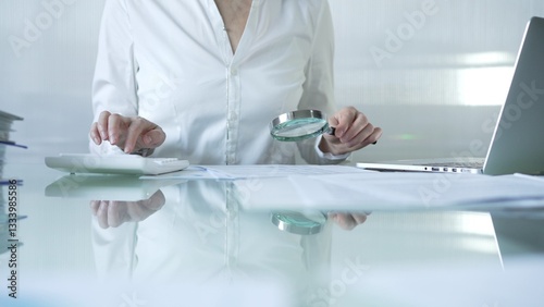 Obraz na płótnie Businesswoman analyzing financial data with magnifying glass and calculator, performing accounting and auditing tasks in office. Audit and taxes theme in business w salonie