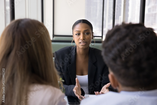 Skilled African financial advisor provides information, consulting young married couple met in bank office. Female applicant passing job interview, answer questions seated in front of two HR managers
