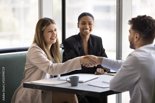 Three multiethnic young 35s businesspeople greeting each other with handshake gesture, met in modern office to conclude agreement, give and receive professional consultation, take part in teamwork