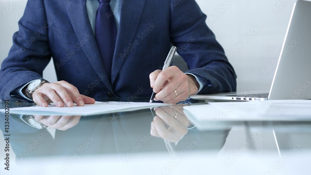 Businessman writing signature on contract with laptop and documents on glass desk in office. Business people concept
