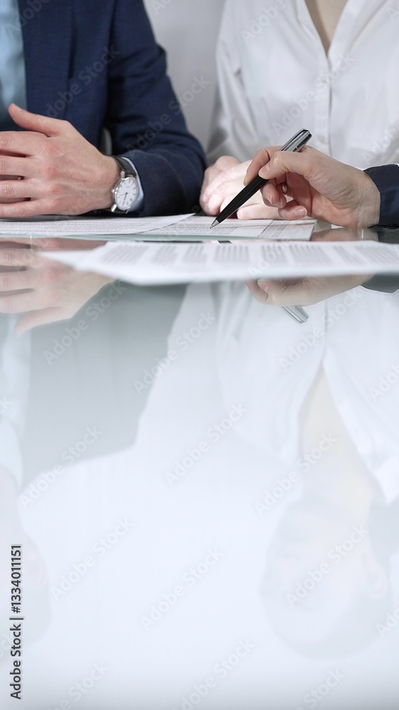 Unrecognizable business people are reviewing contract terms during a meeting while sitting at the glass table in office, vertical close up view. Copy space area Unrecognizable business people are reviewing contract terms during a meeting while sitting at the glass table in office, vertical close up view. Copy space area