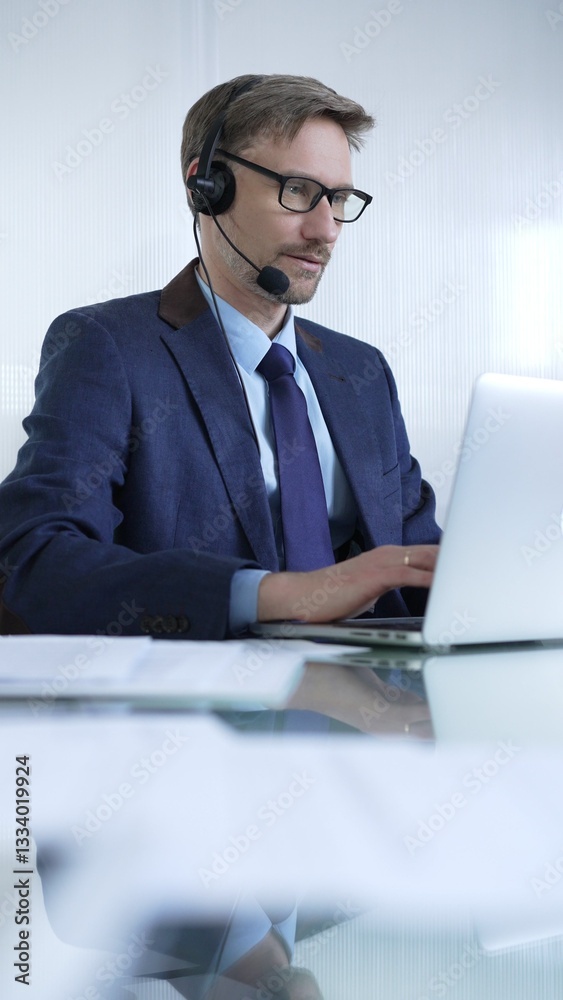 Businessman in blue suit is using a headset and laptop to offer customer service or online consultations. Business people concept
