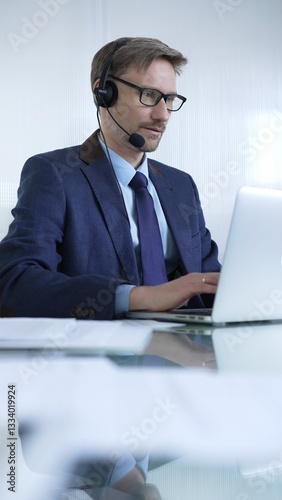 Obraz na płótnie Businessman in blue suit is using a headset and laptop to offer customer service or online consultations. Business people concept w salonie