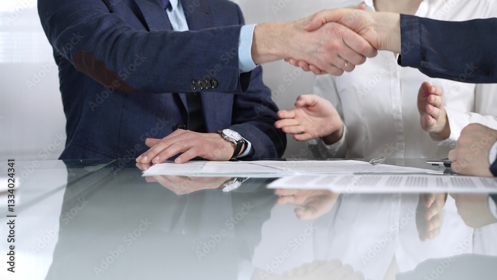 Unrecognizable business partners shaking hands after signing contract at glass table in office meeting, making a deal and closing agreement, close up of handshake