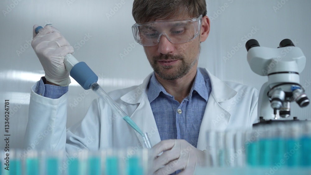 Scientist man wearing a lab coat and safety glasses is using a micropipette to drop a liquid into a test tube, portrait view. Medicine and science