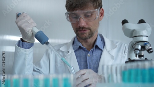 Obraz na płótnie Scientist man wearing a lab coat and safety glasses is using a micropipette to drop a liquid into a test tube, portrait view. Medicine and science w salonie