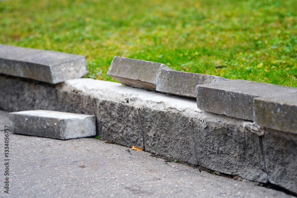 Damaged concrete curb with broken and displaced bricks on city sidewalk, signs of wear, erosion, need for urgent repair in urban infrastructure. Displaced bricks on worn concrete curb. Selective focus