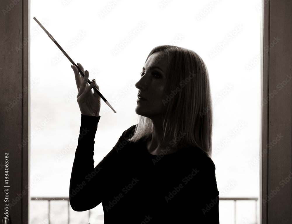 Obraz premium A portrait of a beautiful woman against the light, holding a cigarette holder