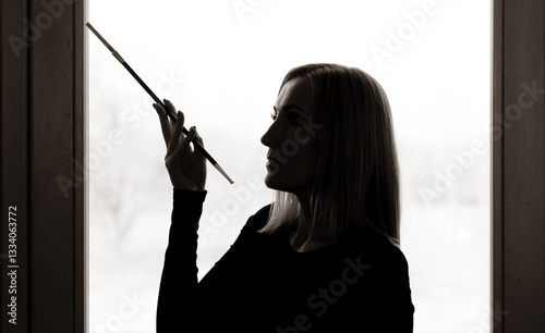 A portrait of a beautiful woman against the light, holding a cigarette holder