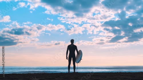 A lone surfer stands contemplating the ocean under a cloudy sky