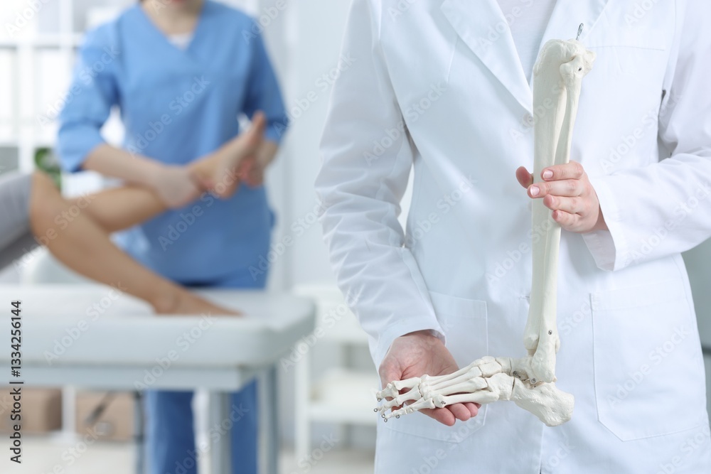 Obraz premium Doctor examining patient's foot in hospital, focus on medical worker with human leg skeleton