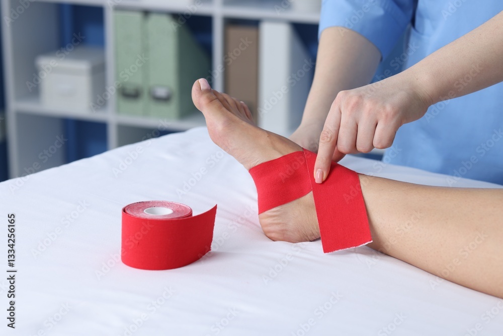 Fototapeta premium Doctor applying kinesio tapes to patient's foot in hospital, closeup
