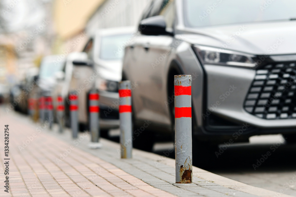 Line of bollards separating the sidewalk from parking lot. Row of red and white striped bollards lines the sidewalk, ensuring safety and controlling traffic in busy urban parking area. Selective focus
